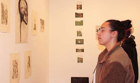 a woman looking at drawings hanging on a wall in the BSU Wallace Anderson Art Gallery